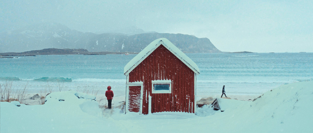 A red cabin by the sea with two distant figures